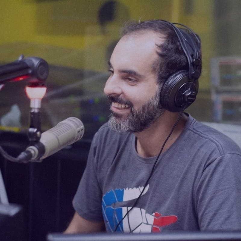 Thiago Cordeiro de fones de ouvido, sorrindo diante do microfone no estúdio.